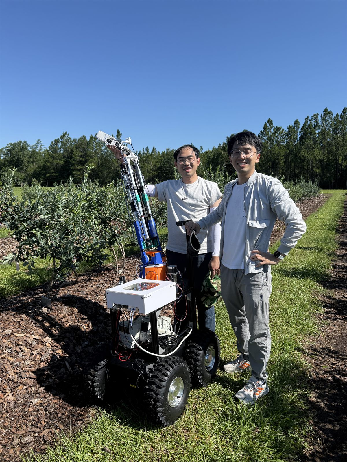 Two members of the project team standing beside the harvesting robot in a blueberry field